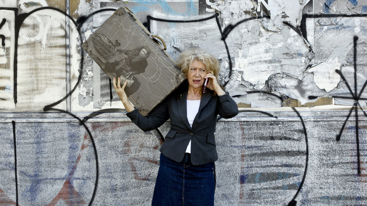 Woman balances suitcase and takes call. On suitcase, a photo of the Woman with trolley of things she has collected.